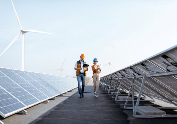 Two engineers examining solar panels on a rooftop with windmills in the distance