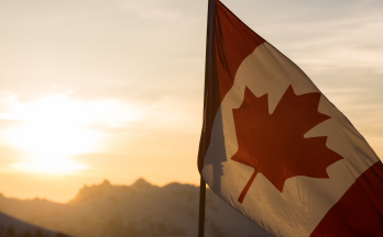 Canadian flag in front of sun and mountains Canadian flag in front of sun and mountains
