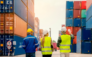 Three people wearing safety vest and hard hats looking at multiple shipping containers