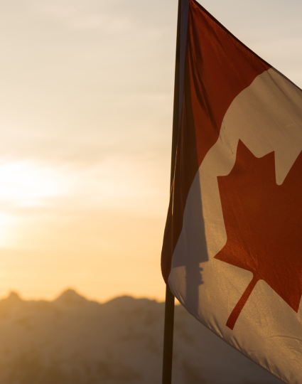 Canadian flag in front of sun and mountains