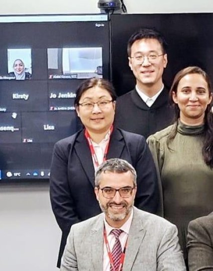 Group photo of peer evaluation participants in New Zealand, with virtual attendees visible on screen.
