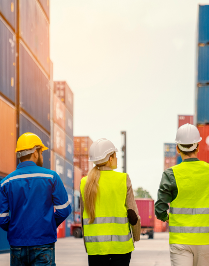 Three people wearing safety vest and hard hats looking at multiple shipping containers