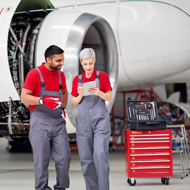 A man and a woman wearing overalls in front of a plane propeller