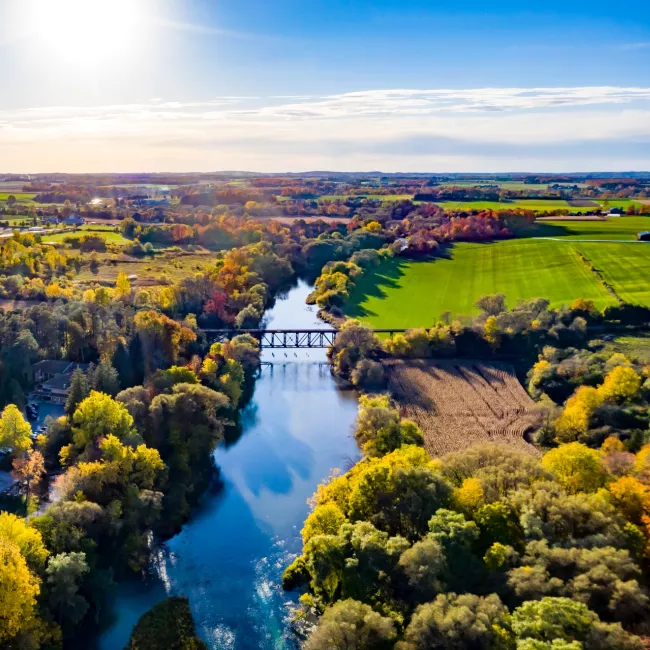 Aerial view of fields, forest and a river with bridge across it