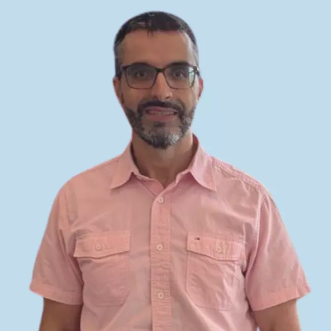 Headshot of Abdel Kassou wearing a salmon coloured button up shirt over a light blue background