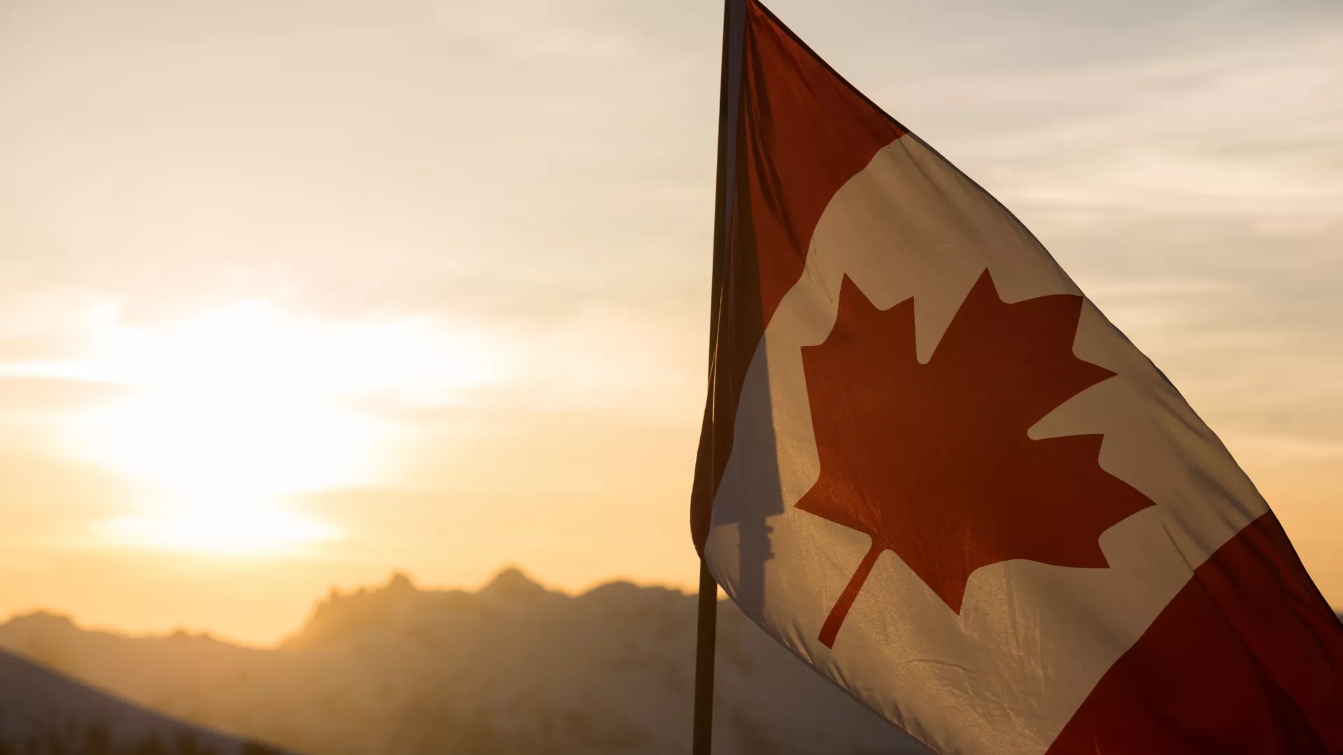 Canadian flag in front of sun and mountains