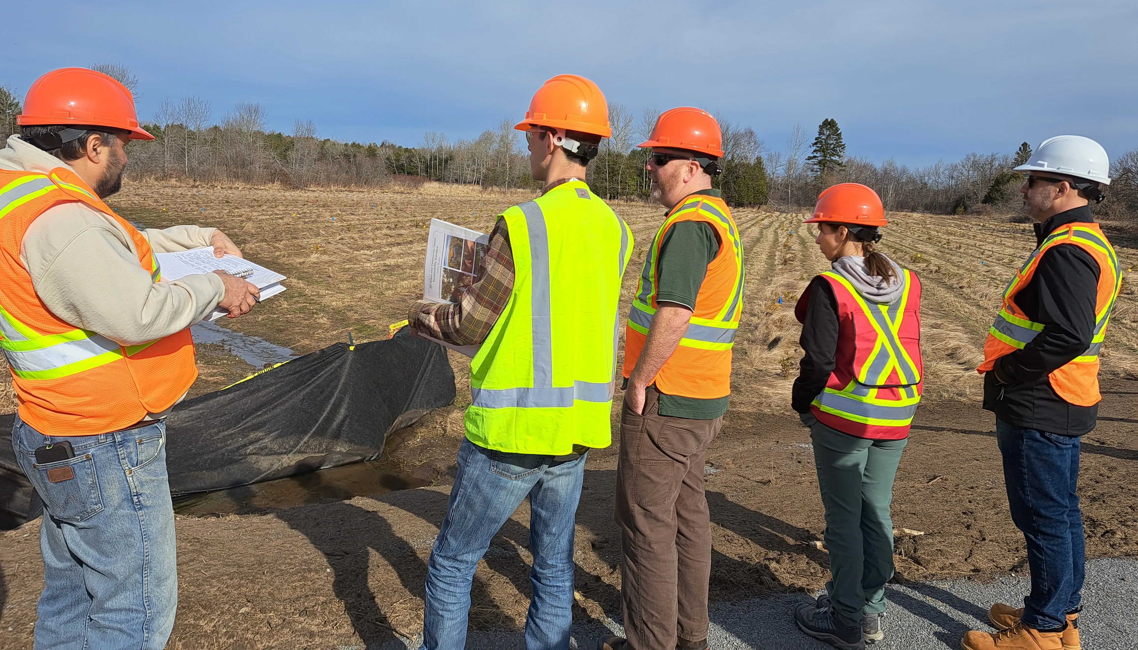 Assessment team in safety gear reviewing documents at a field site. Assessment team in safety gear reviewing documents at a field site.
