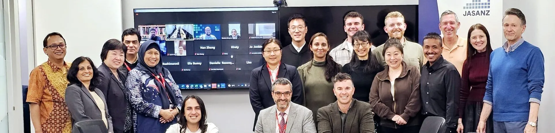 Group photo of peer evaluation participants in New Zealand, with virtual attendees visible on screen.