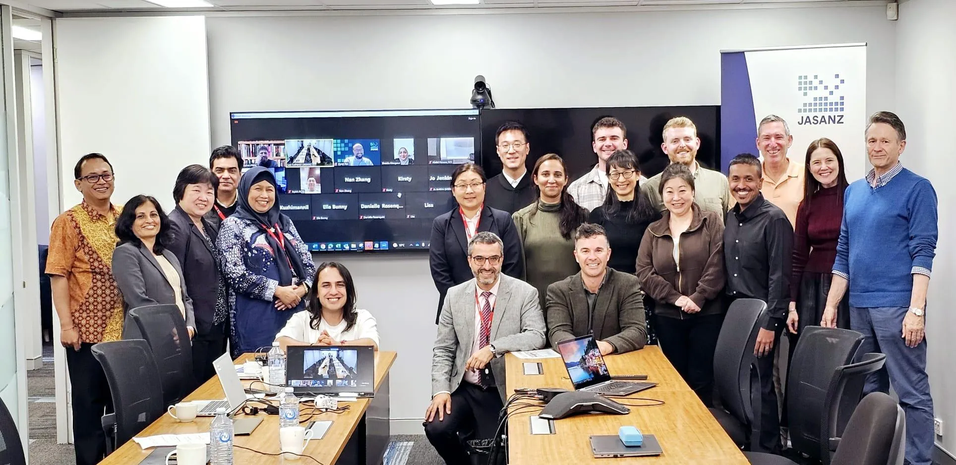 Group photo of peer evaluation participants in New Zealand, with virtual attendees visible on screen. Group photo of peer evaluation participants in New Zealand, with virtual attendees visible on screen.