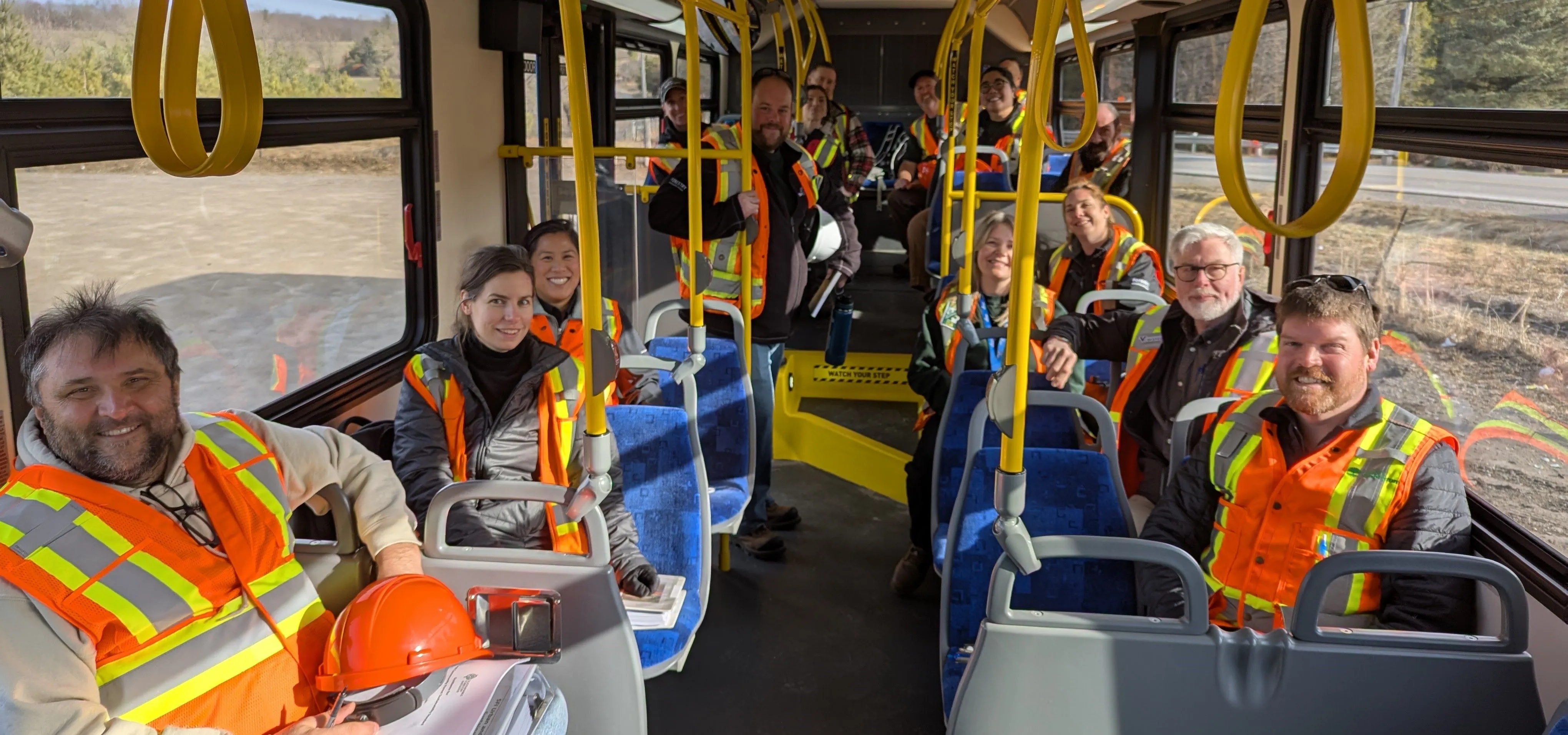 Assessment team in safety gear smiling inside a transit bus during a site tour.