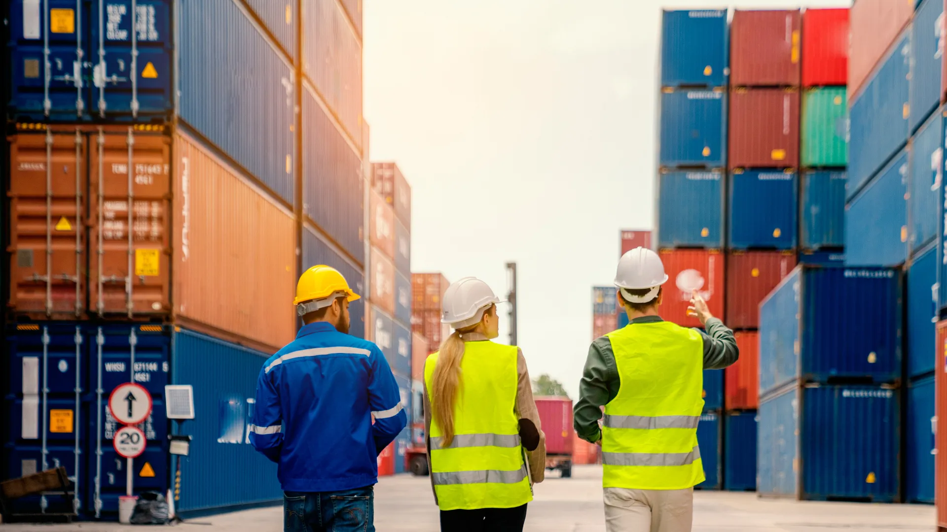Three people wearing safety vest and hard hats looking at multiple shipping containers